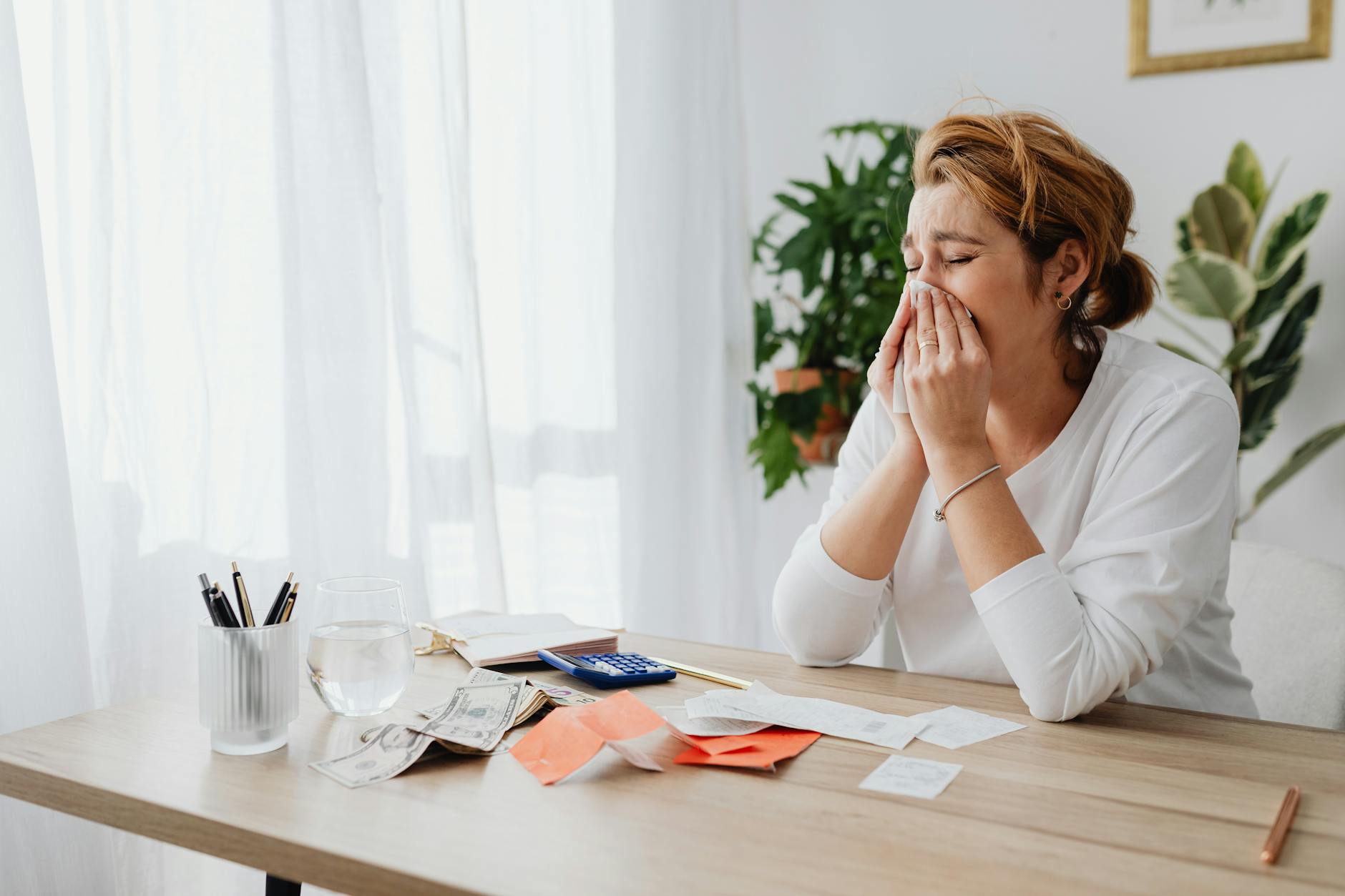 Woman looking stressed while managing finances at her office desk with papers and calculator.