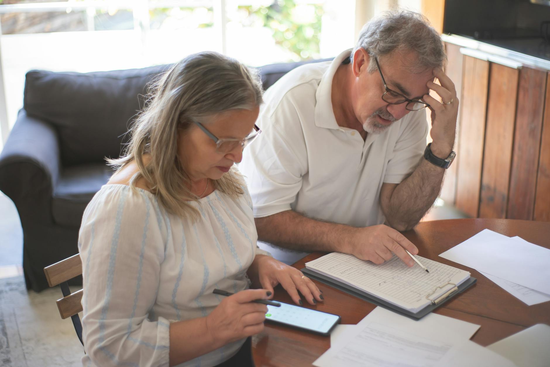 Elderly couple reviewing bills and documents at home, focusing on finances and technology.