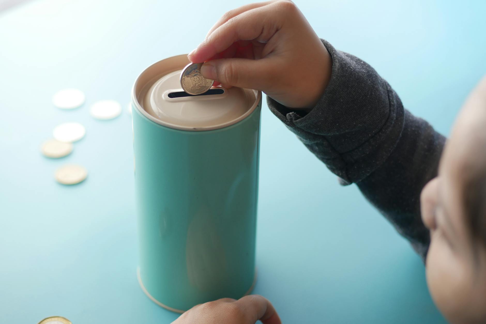 Child placing coins into a piggy bank, illustrating saving and investing for a child's future