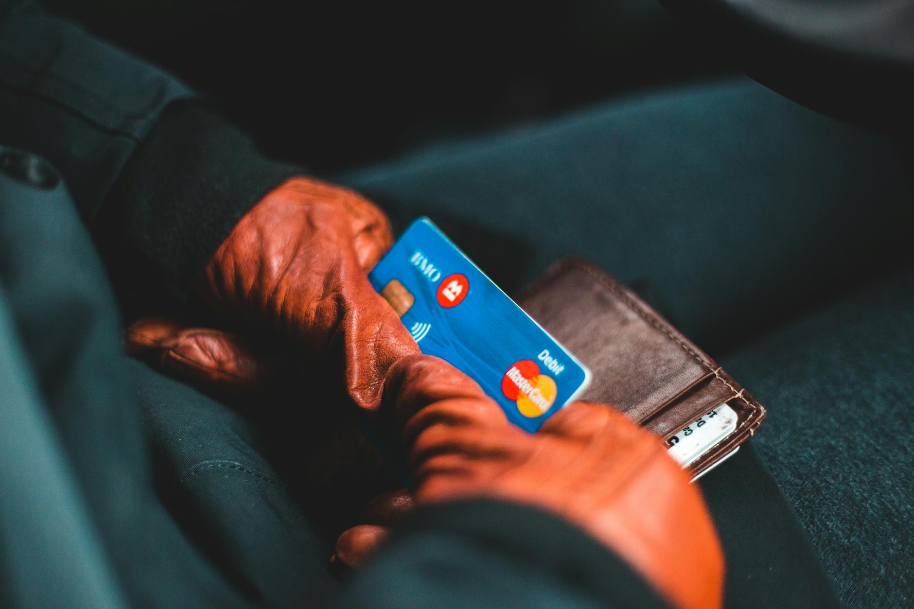Person holding a debit card while looking at a banking app on a phone, illustrating Regulation E debit card fraud rights