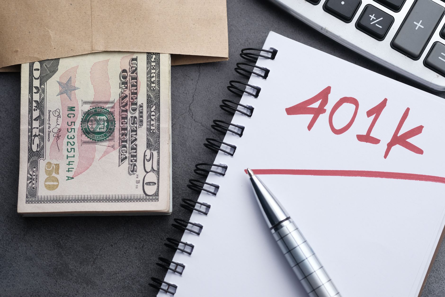 A desk with a notebook labeled 401k, a calculator, cash and a pen