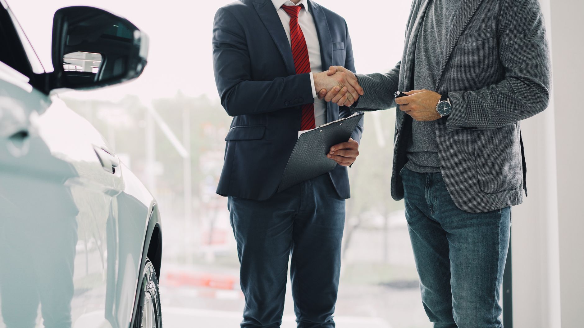 Buyer signing car loan financing paperwork at a dealership desk with car keys