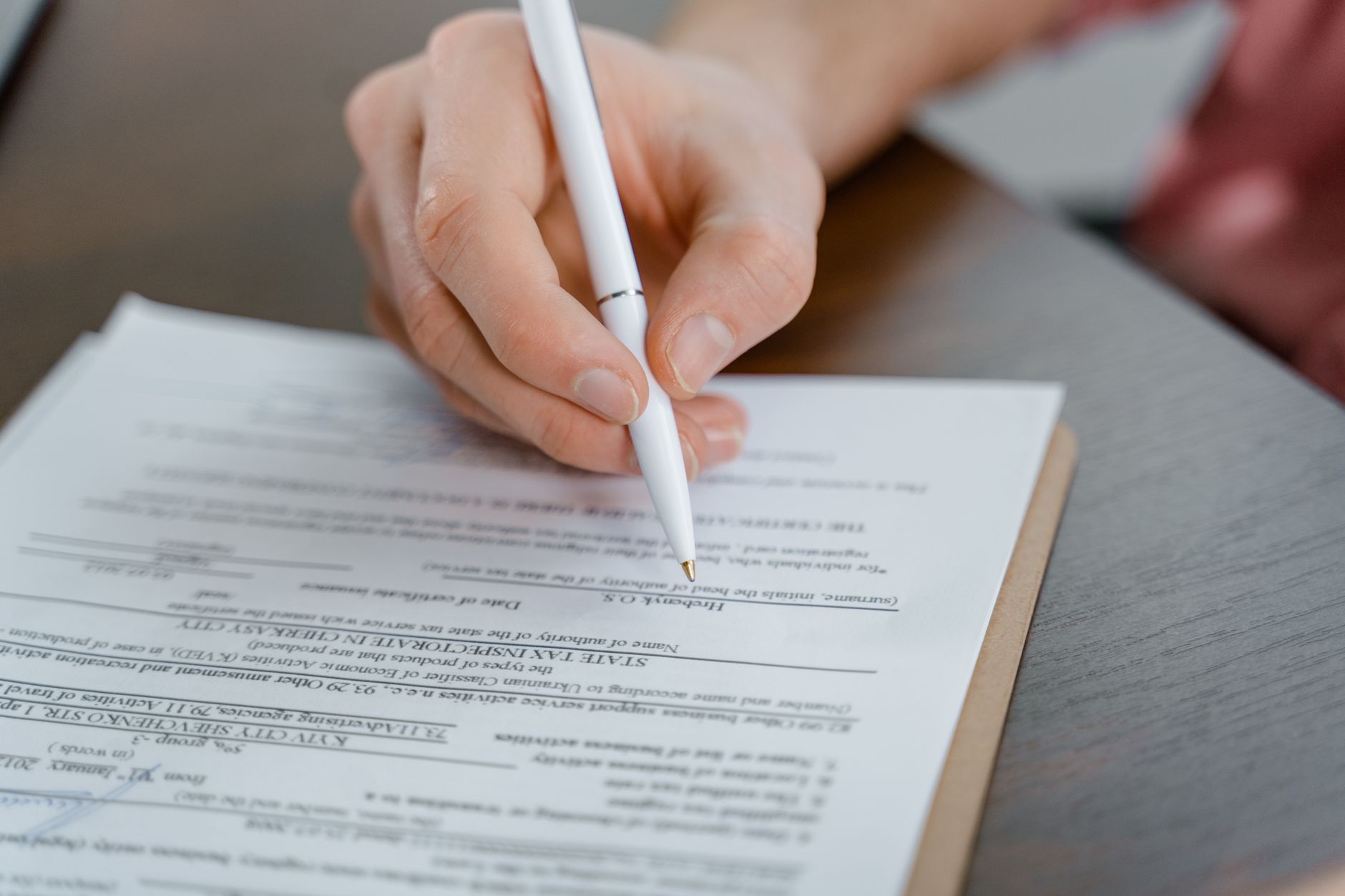 Hands signing a beneficiary designation form at a desk with a pen